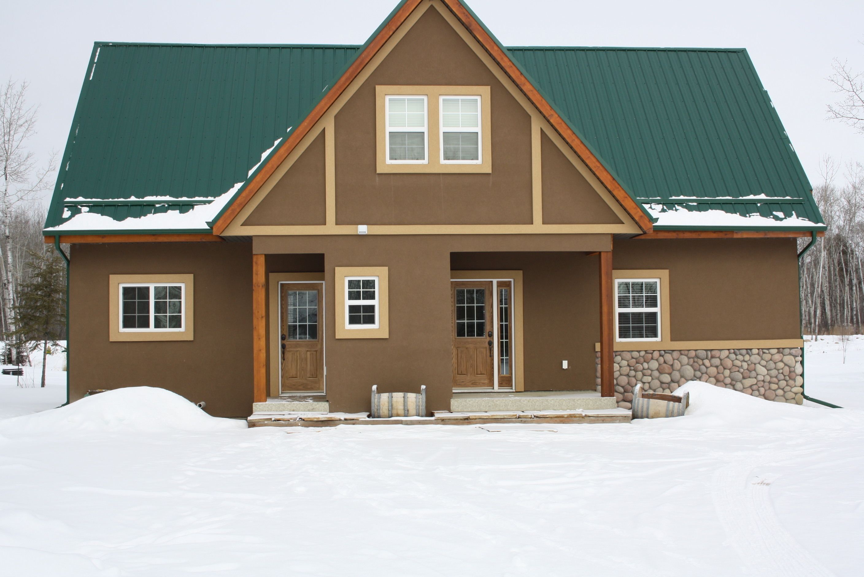 A two-story house with a green roof, brown siding, and a stone foundation.
