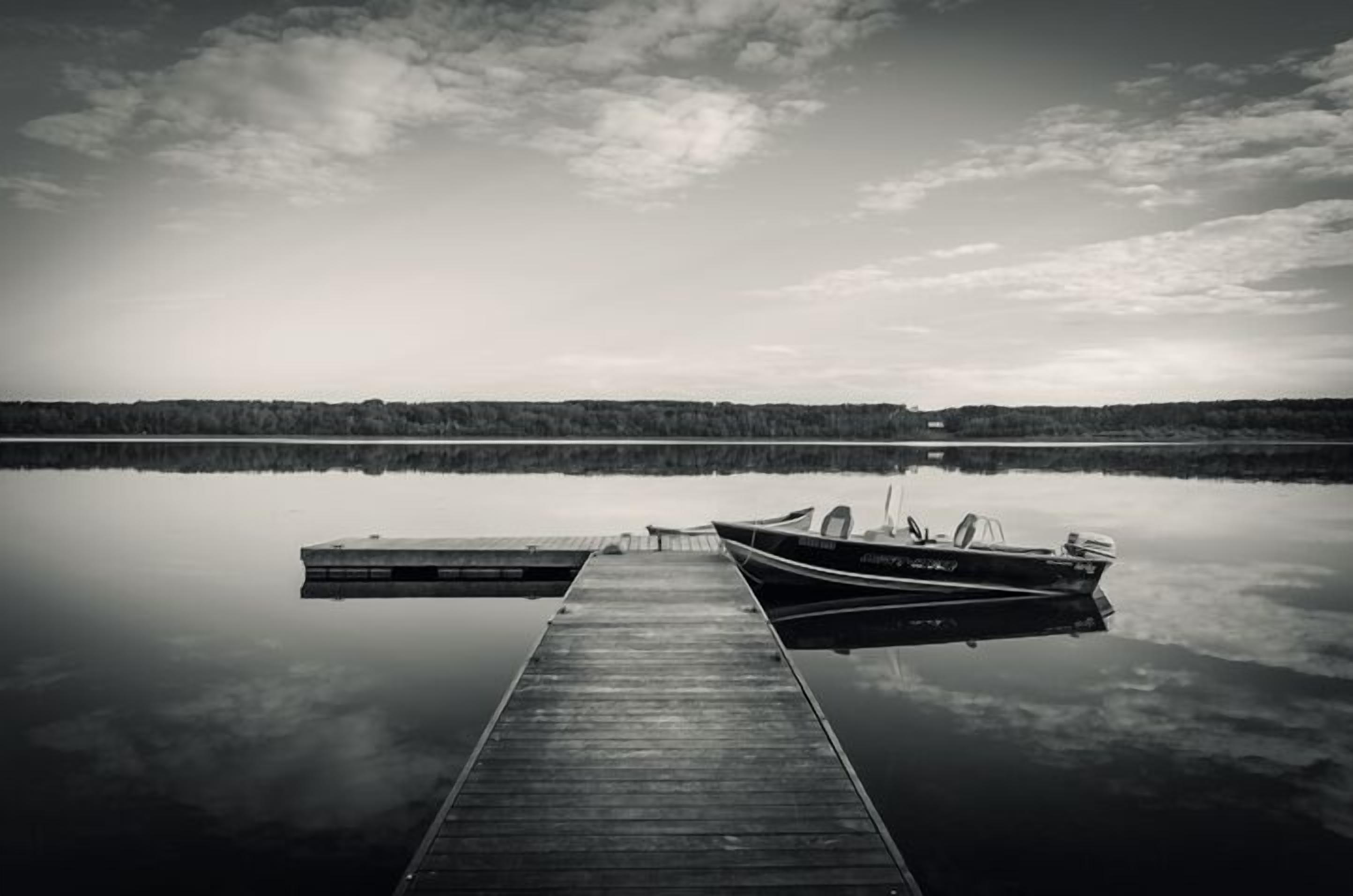 A wooden dock extending into calm water with a boat moored at the end.
