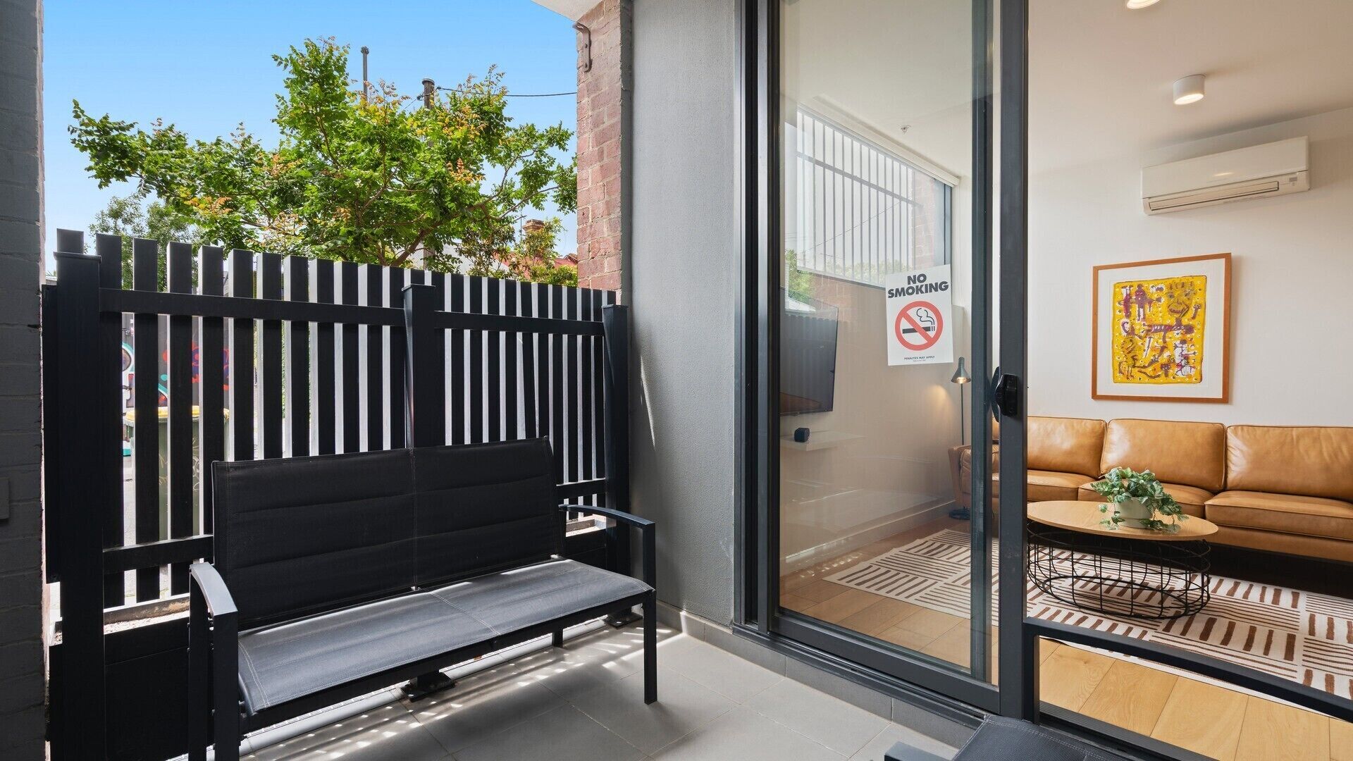 A modern interior with a black bench, a glass door leading to a room with a sofa and a "NO SMOKING" sign.