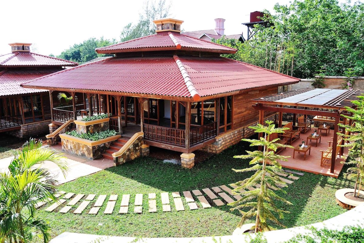 Un edificio tradicional de madera con techo rojo, un patio cubierto con mobiliario de madera y una escalera de piedra que conduce a la entrada.