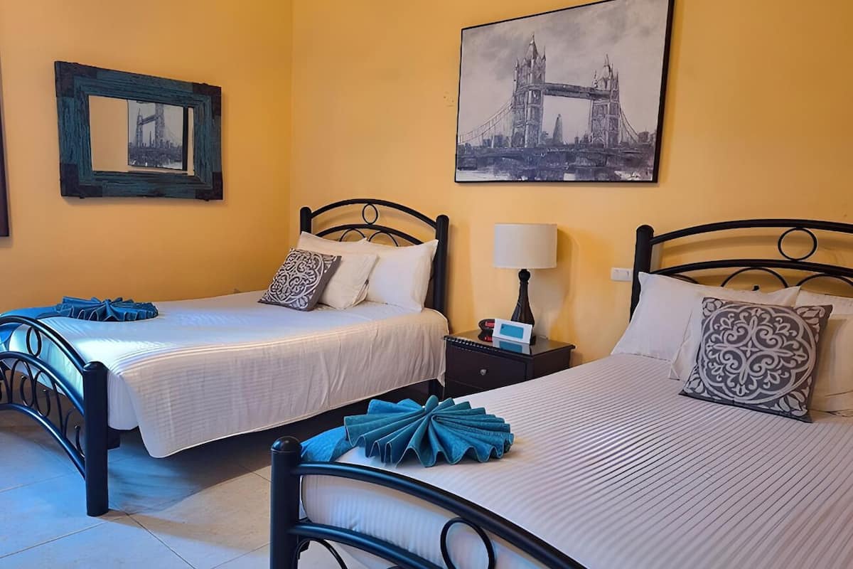 A hotel room with two beds, a nightstand, a lamp, and a framed picture of a bridge on the wall.