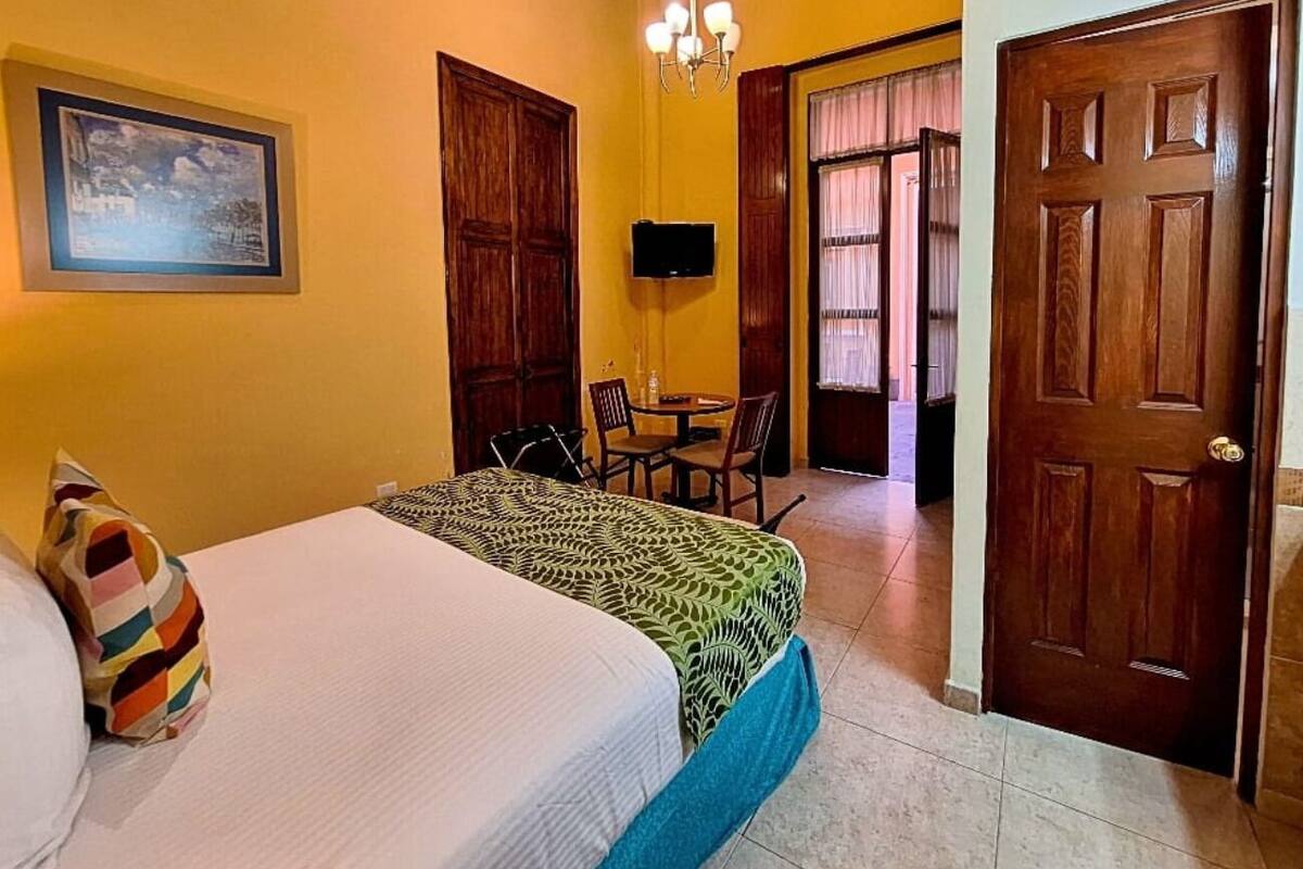 A hotel room with a bed, a TV, a dining table with chairs, and a wooden door.