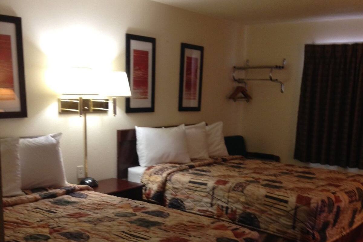 A hotel room with two beds, a nightstand, a lamp, and framed pictures on the wall.