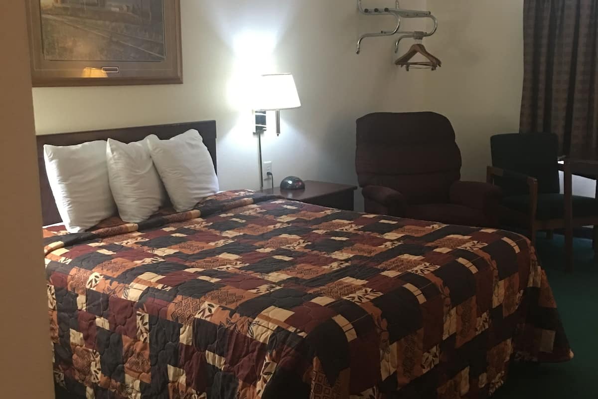 A hotel room with a large bed, a desk, a chair, a lamp, and a coat rack.