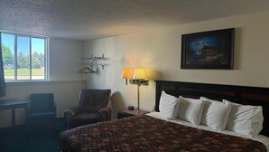 A hotel room with a large bed, a chair, a desk, a lamp, and a painting on the wall. - Mobridge Kountry Inn (Mobridge)