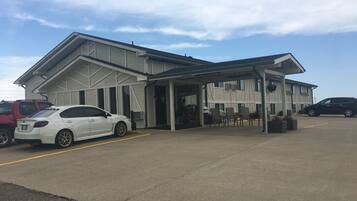 Un edificio con un acceso cubierto, un estacionamiento y algunos coches aparcados.