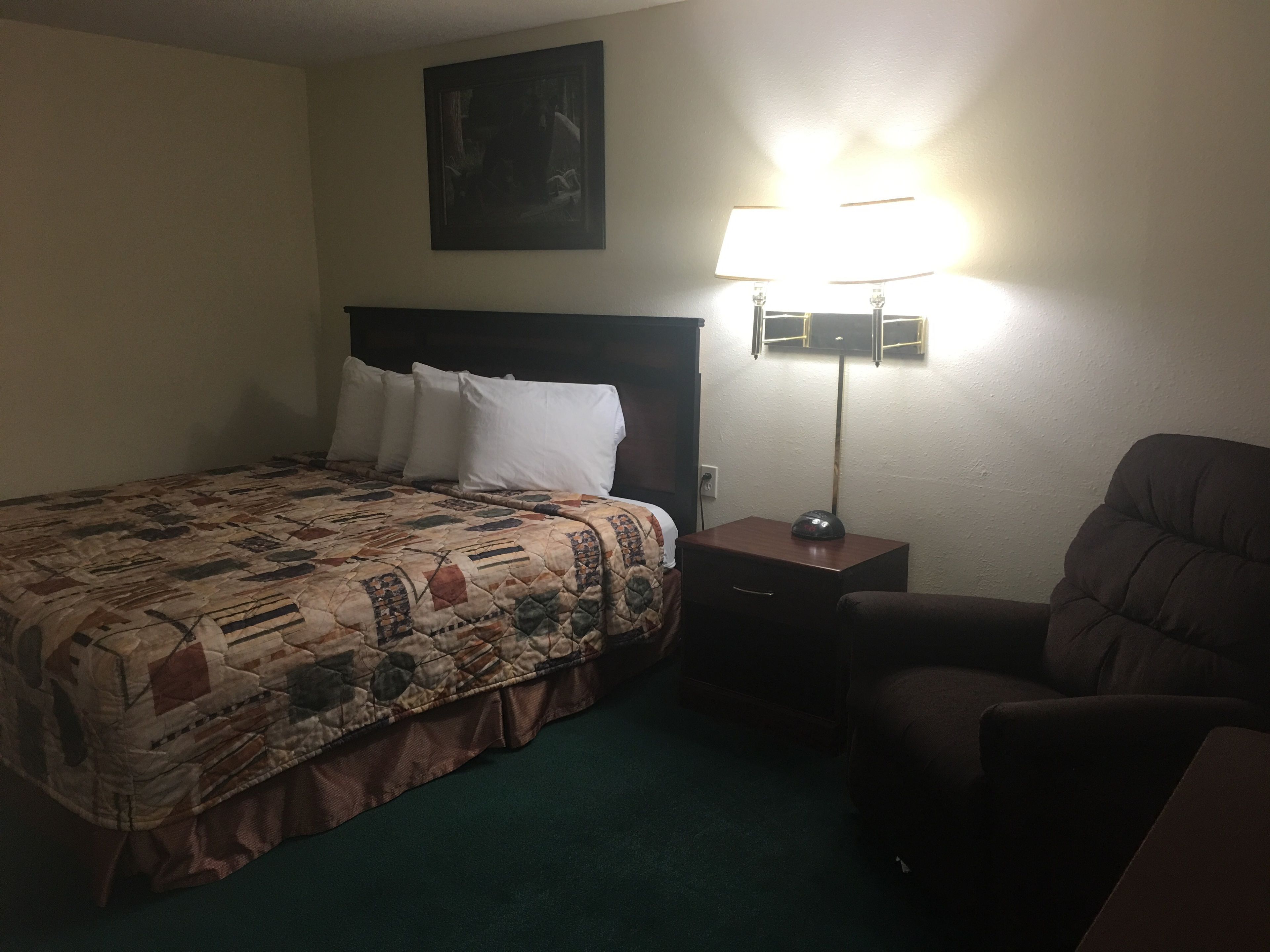 A hotel room with a bed, a chair, a nightstand, and a lamp.