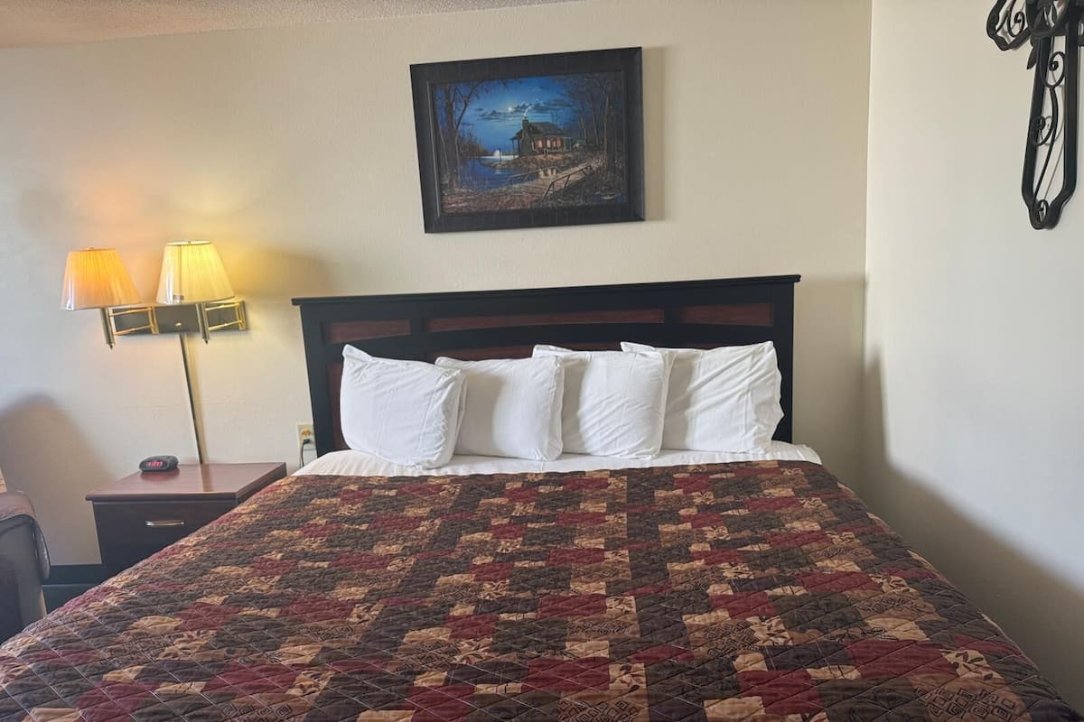 A neatly made bed with a patterned quilt, a nightstand with a lamp, and a painting on the wall.