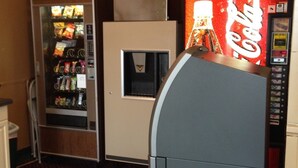 A vending machine with a Coca-Cola logo, a refrigerator, and a snack vending machine in a room with patterned carpet. - Mobridge Kountry Inn (Mobridge)