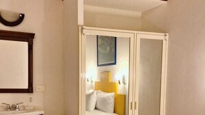 Hotellihuone, jossa on sänky, yöpöytä, peili ja vaatekaappi.