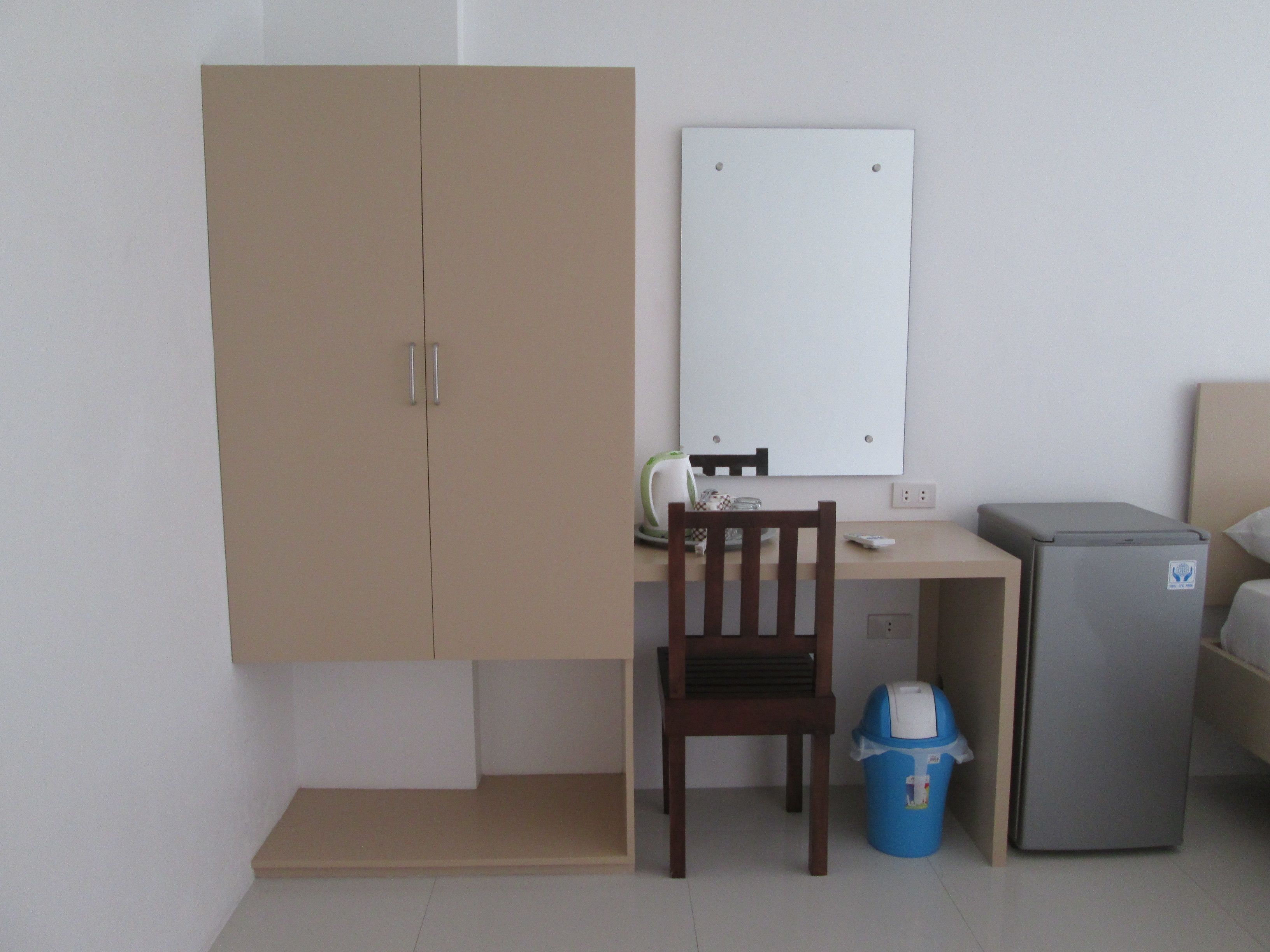 A small room with a desk, a chair, a cabinet, a refrigerator, and a trash bin.
