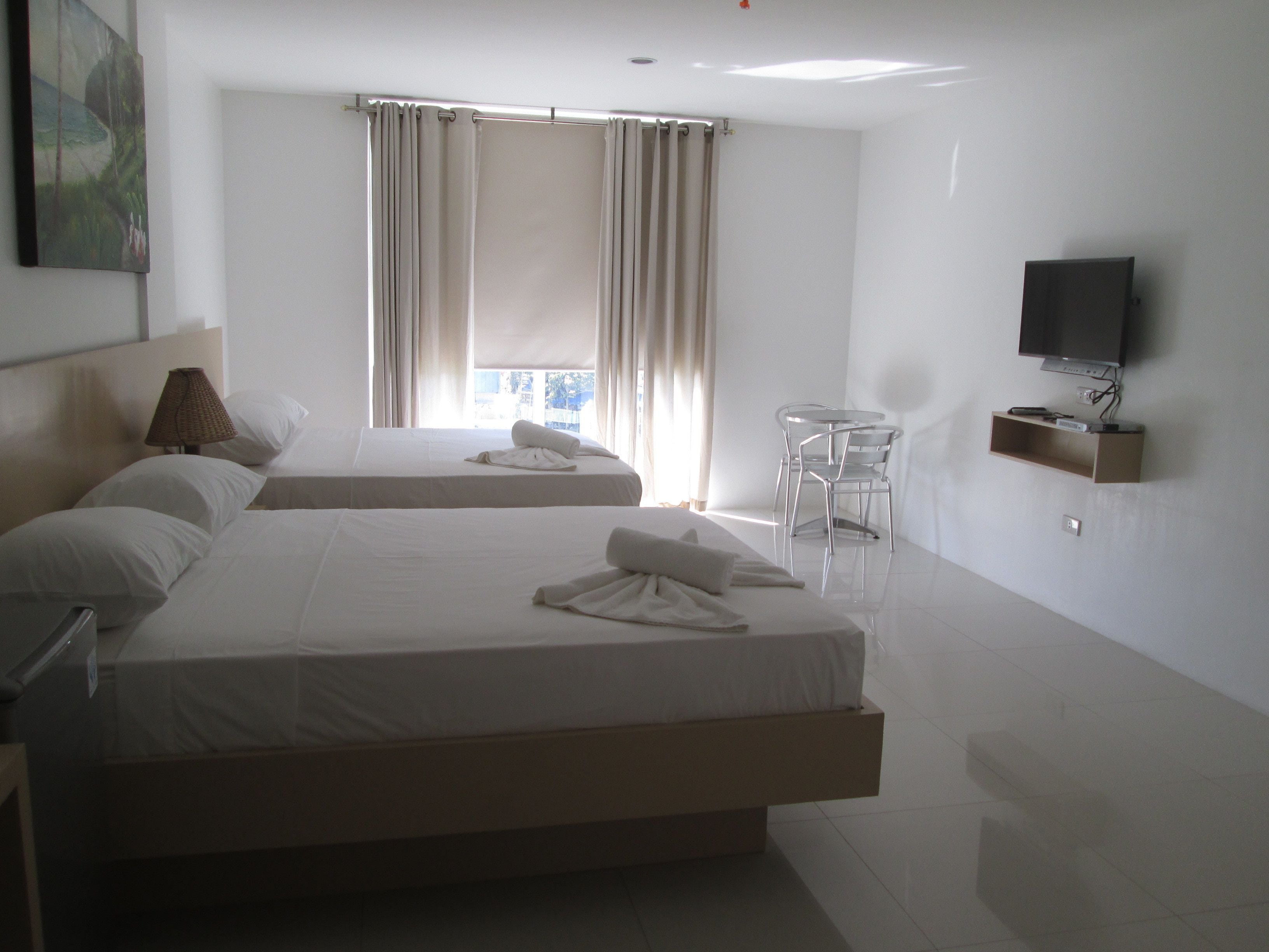 A hotel room with two beds, a TV, a small table, and a window with curtains.