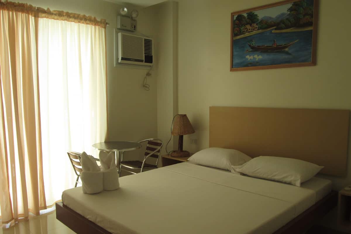A hotel room with a bed, a table with chairs, a lamp, and a painting on the wall.