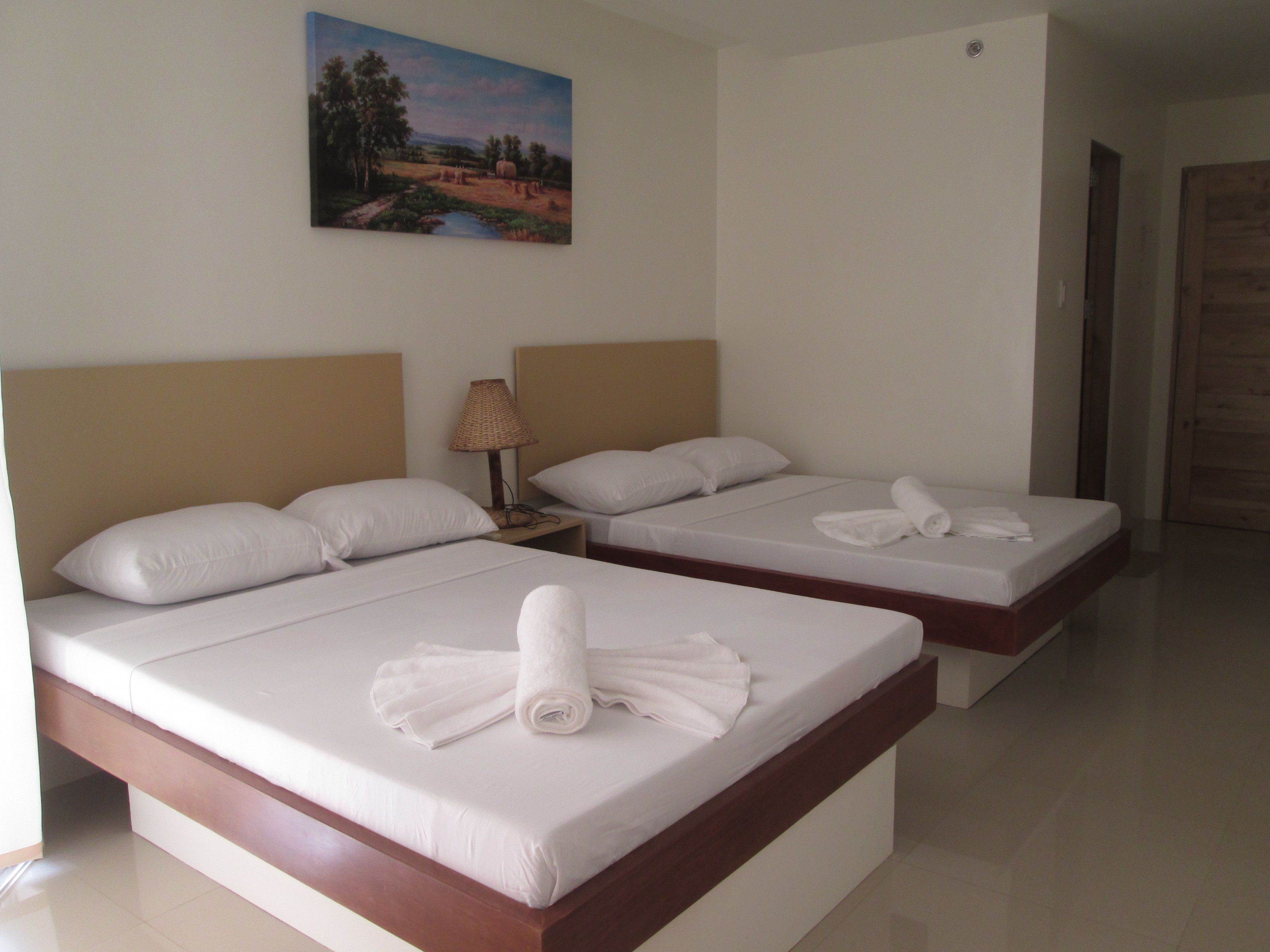 Ein Hotelzimmer mit zwei Betten, jeweils mit weißer Bettwäsche und Handtüchern, einem Gemälde an der Wand und einer Holztür.