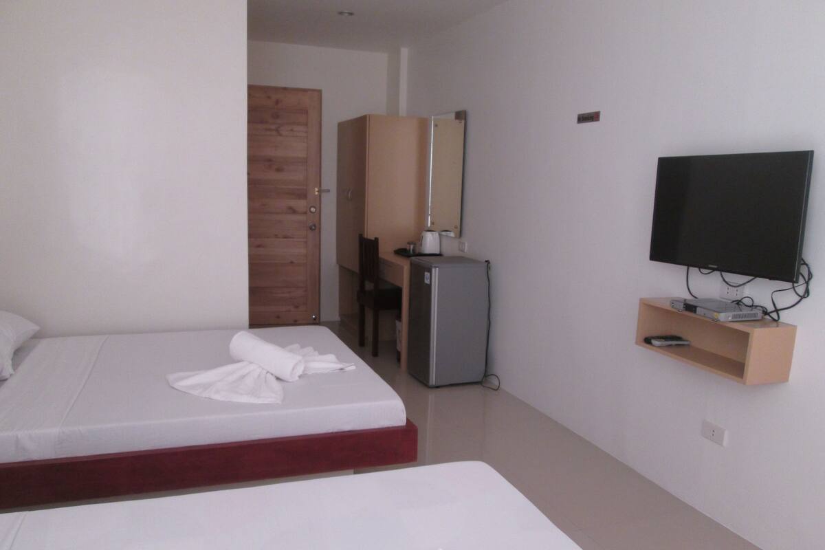 A hotel room with two beds, a desk, a television, and a small refrigerator.