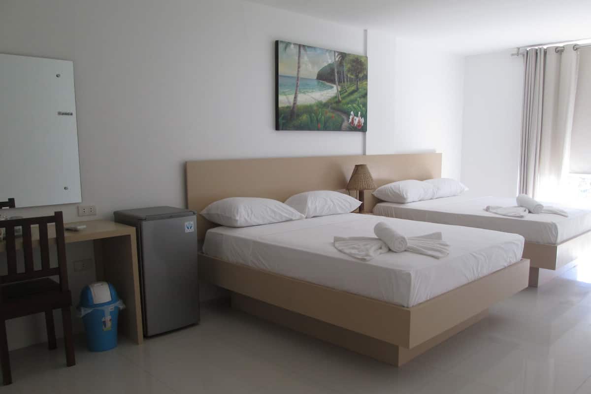 A hotel room with two beds, a desk, a small refrigerator, and a trash bin.