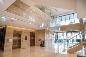 A modern hotel lobby with a glass staircase, elevators, and a reception desk.