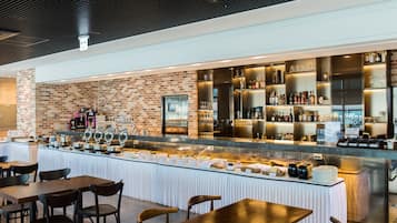 A modern bar area with a brick wall, a long counter with various bottles and glasses, and several tables and chairs for dining.