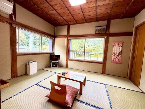 A traditional Japanese room with tatami flooring, a tatami mat table, a television, and a small heater.