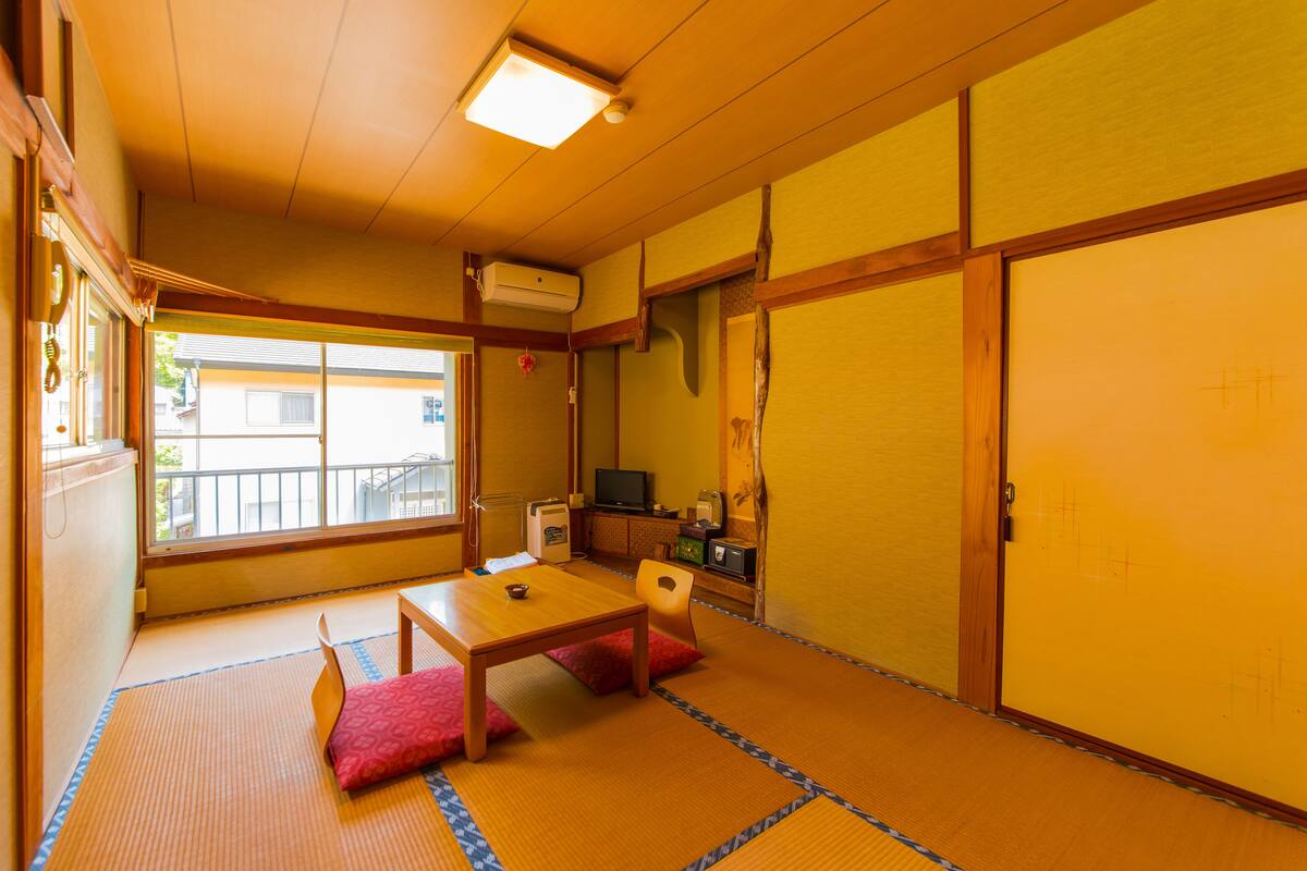 Una habitación japonesa tradicional con suelo de tatami, una mesa baja, cojines, un televisor y una puerta corredera.