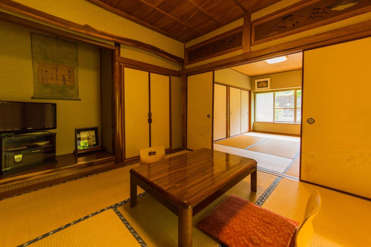 Una habitación japonesa tradicional con suelo de tatami, una mesa de madera, un televisor y puertas correderas.