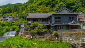 A traditional Japanese house with a stone wall and a small waterfall in the background. - Takaosou (Yufu)
