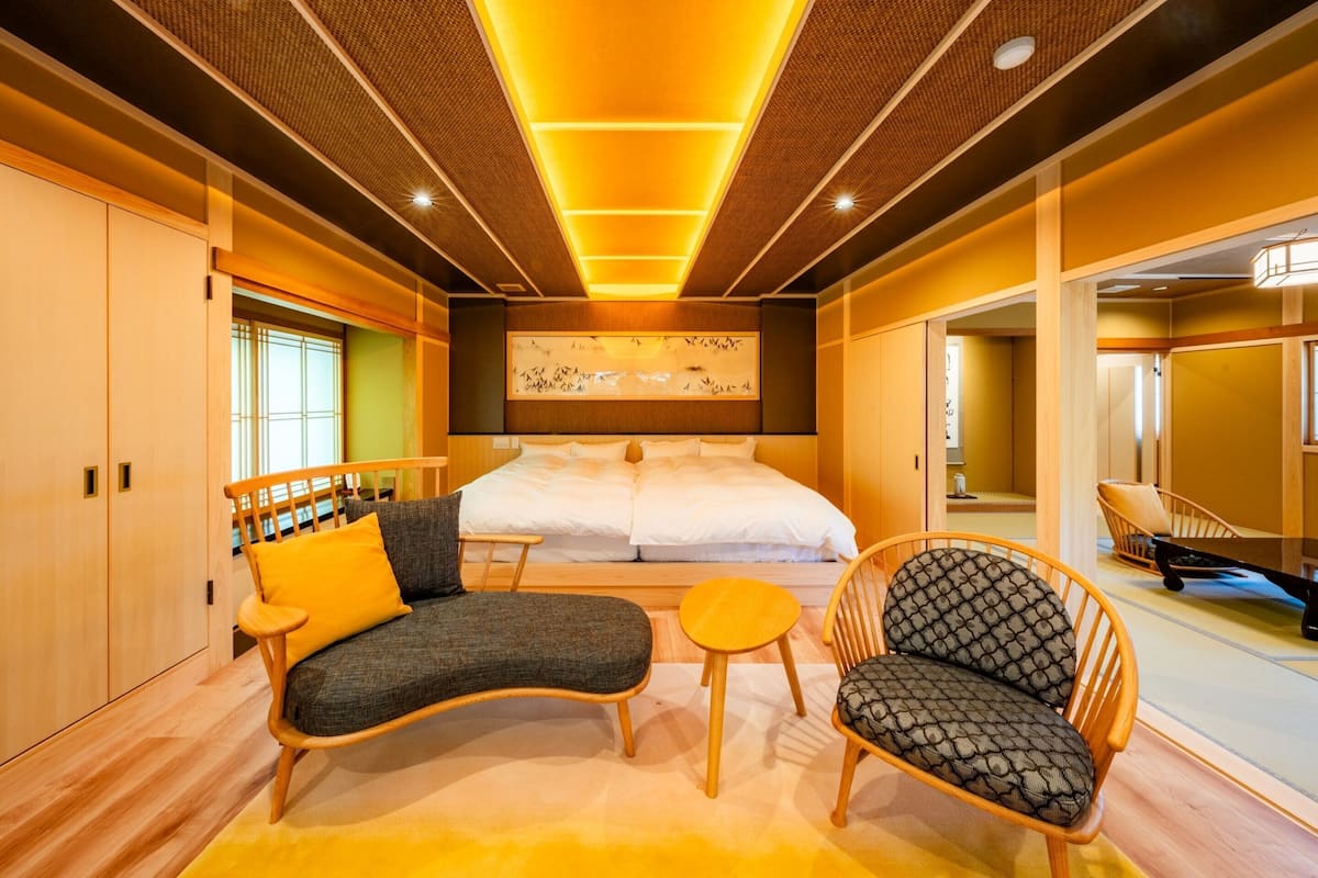 A modern hotel room with a large bed, a sofa, two chairs, and a small table.