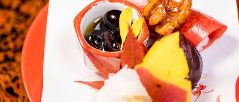 A plate with a variety of food items including a bowl of olives, a piece of fruit, and a nut.