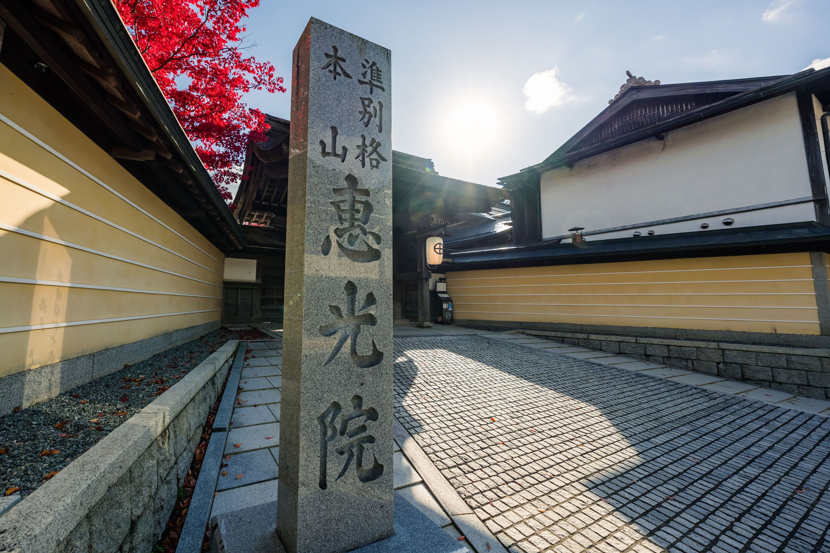 A stone monument with Japanese characters, a traditional building with a tiled roof, and a pathway with a stone border.