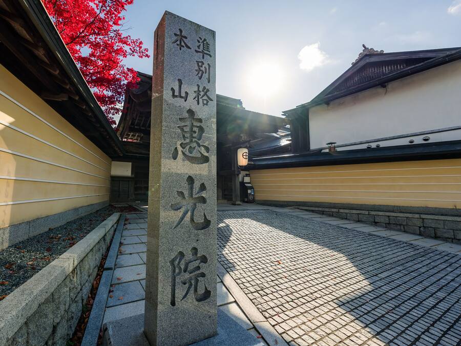 A stone monument with Japanese characters, a traditional building with a tiled roof, and a pathway with a stone border.