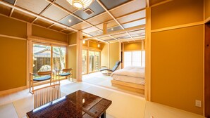A traditional Japanese-style room with tatami flooring, a low wooden table, a futon bed, and sliding doors leading to an outdoor area.