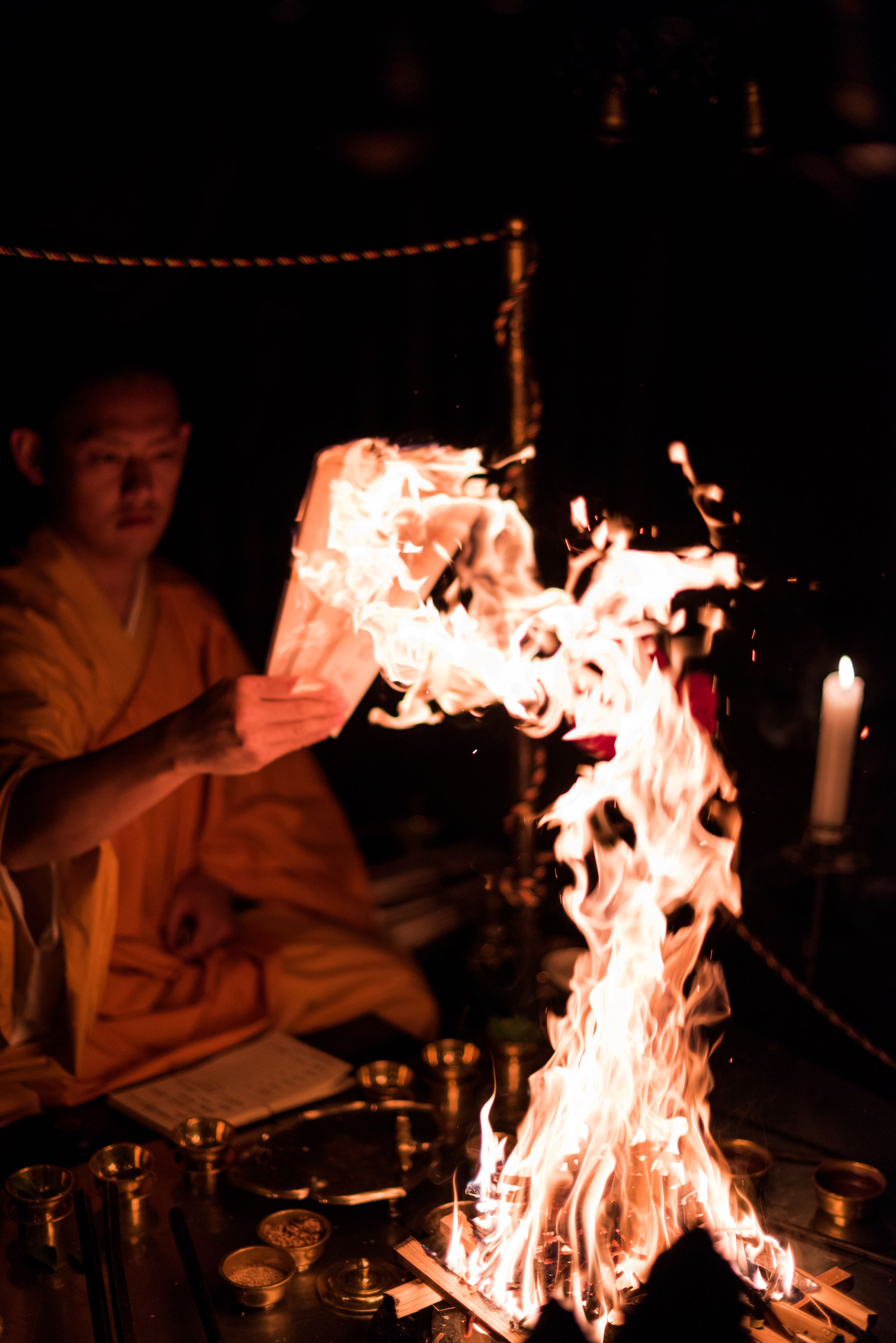 A person performing a ritual with fire, surrounded by ritualistic items and a candle.
