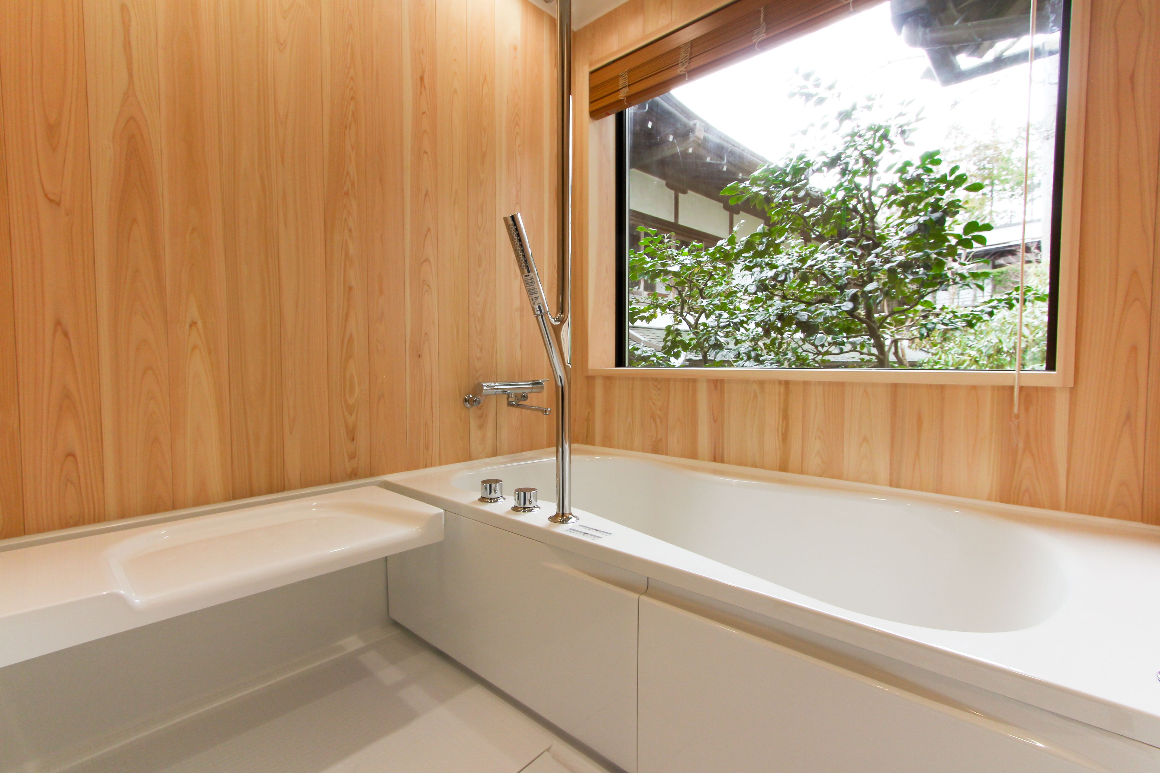 A modern bathroom with a wooden wall, a large bathtub, and a window with a view of trees.