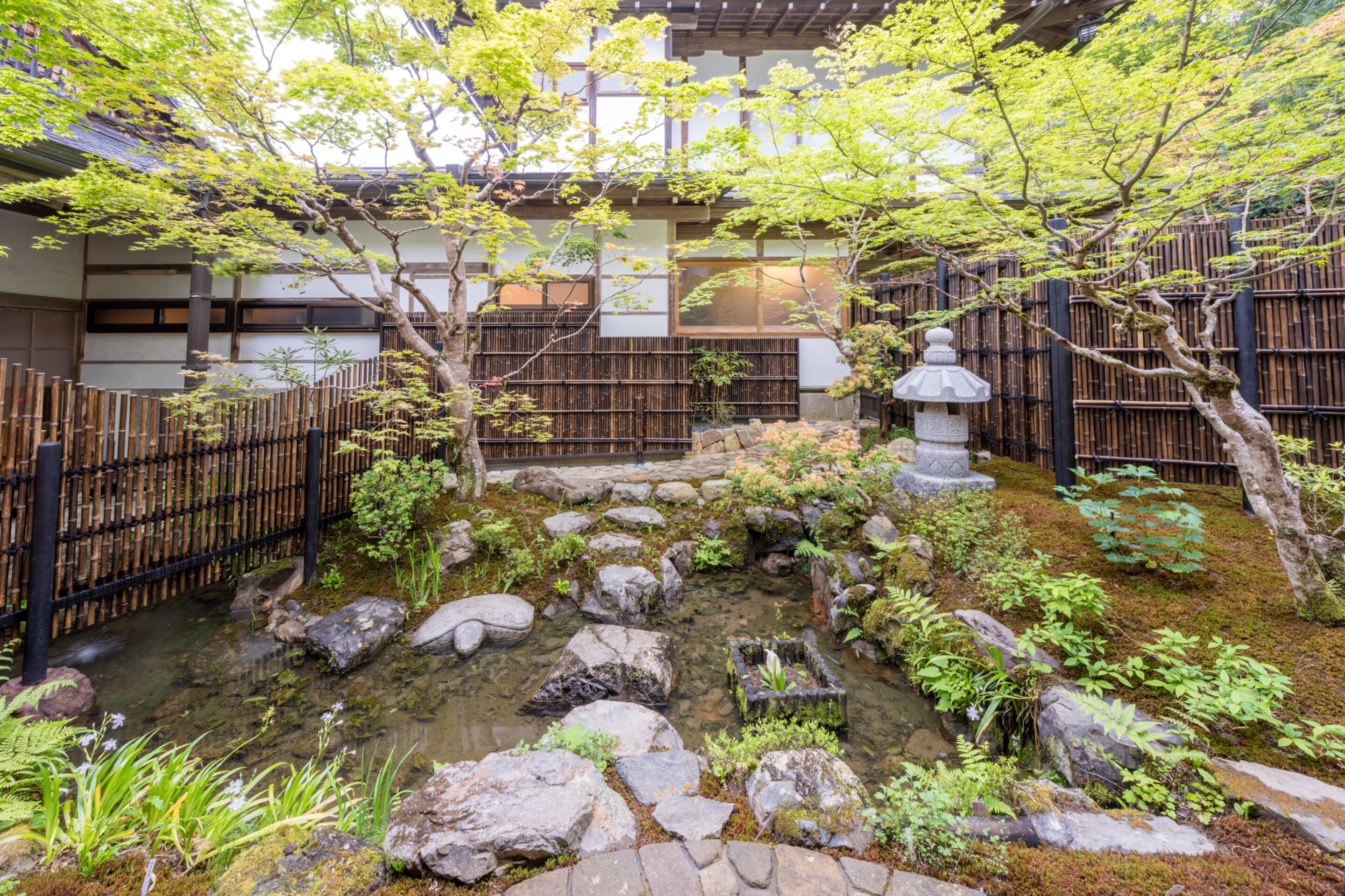 Un jardín japonés tradicional con un estanque de carpas, una valla de bambú y un farol de piedra.