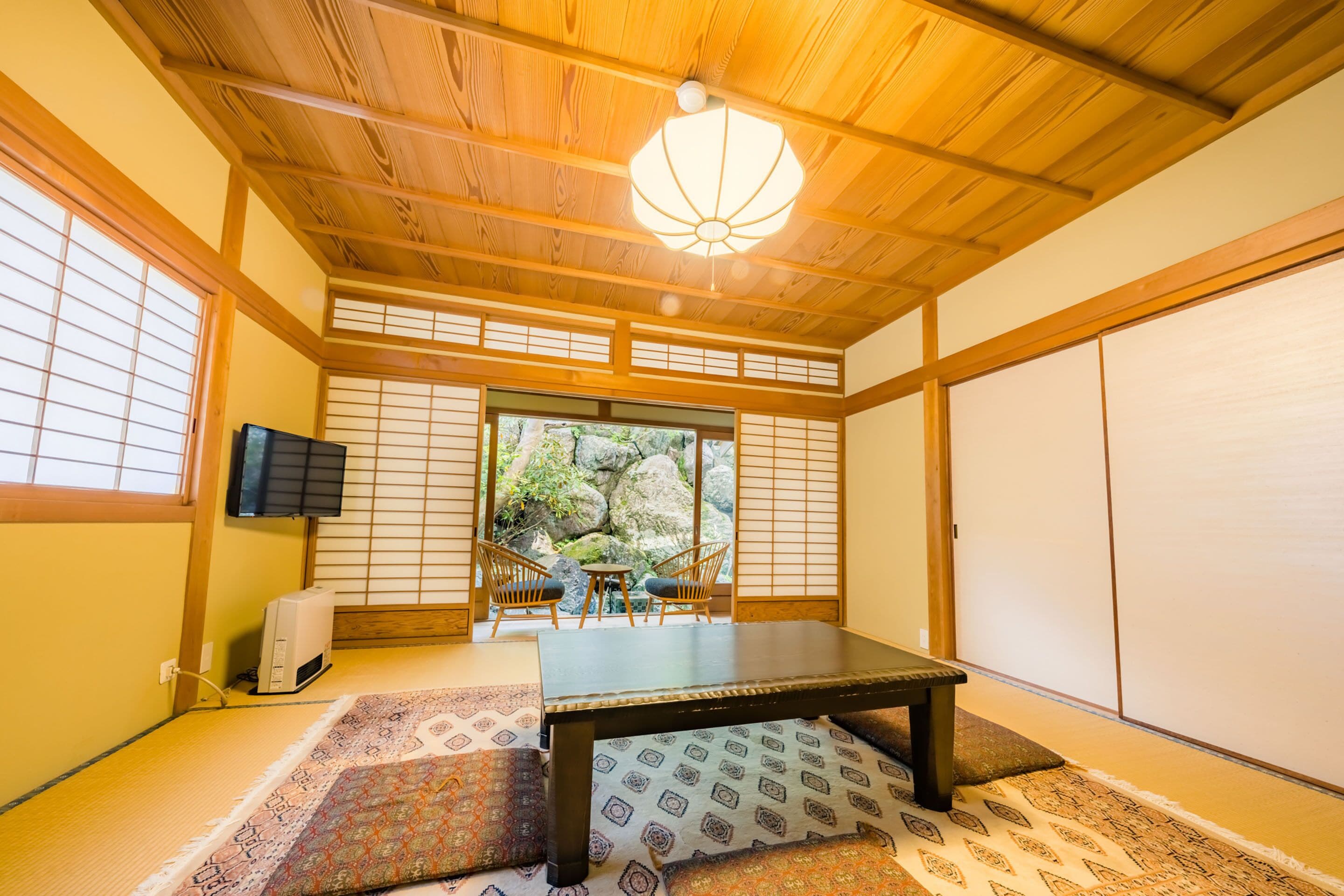 A traditional Japanese room with tatami flooring, a low table, sliding doors, and a view of a garden.