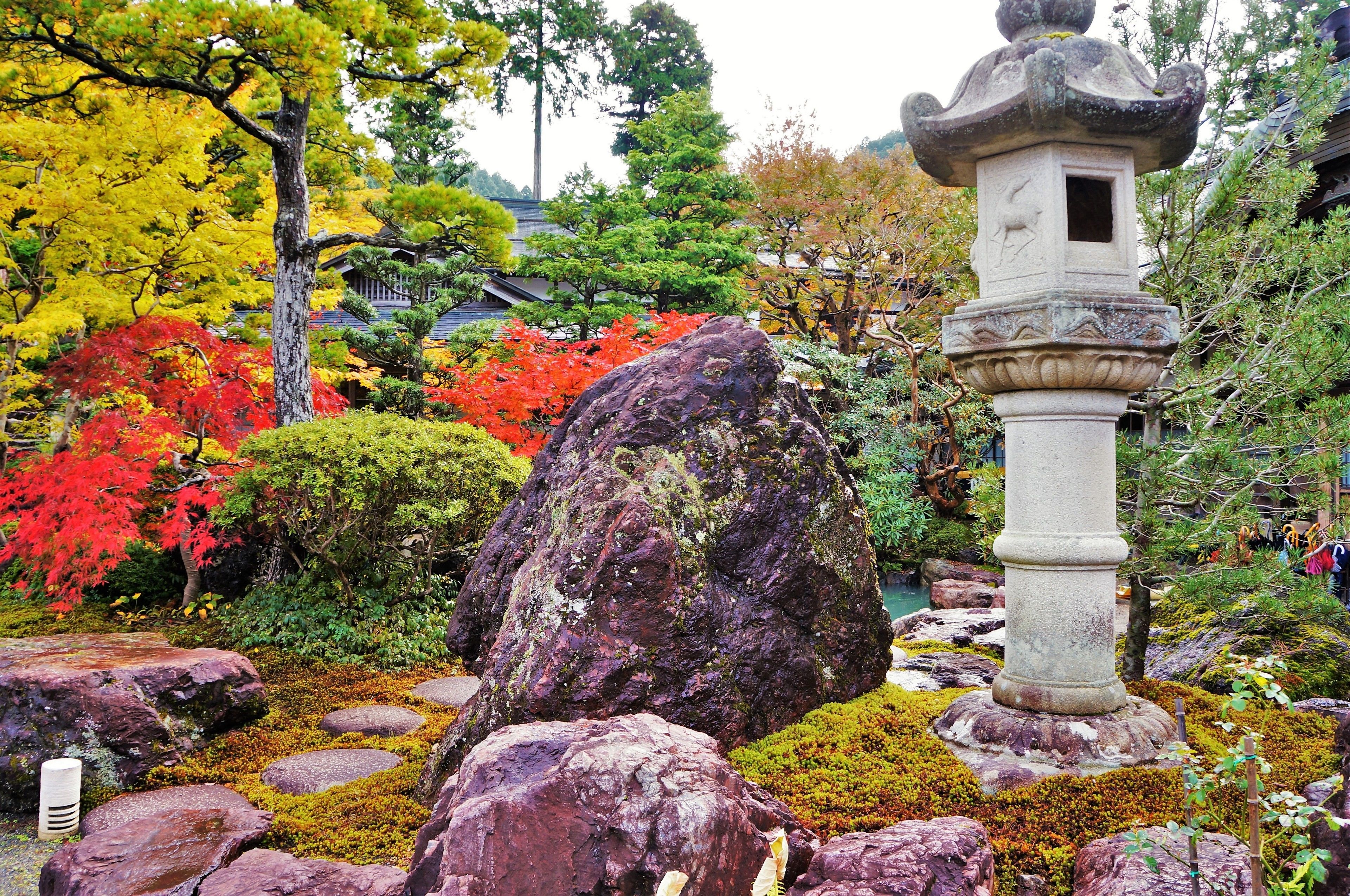 A traditional Japanese garden with a stone lantern, large rocks, and colorful foliage.