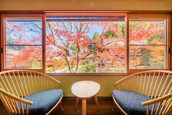 A room with two wooden chairs and a small table, a large window with a view of autumn trees. - Koyasan Syukubo Ekoin (Koya)