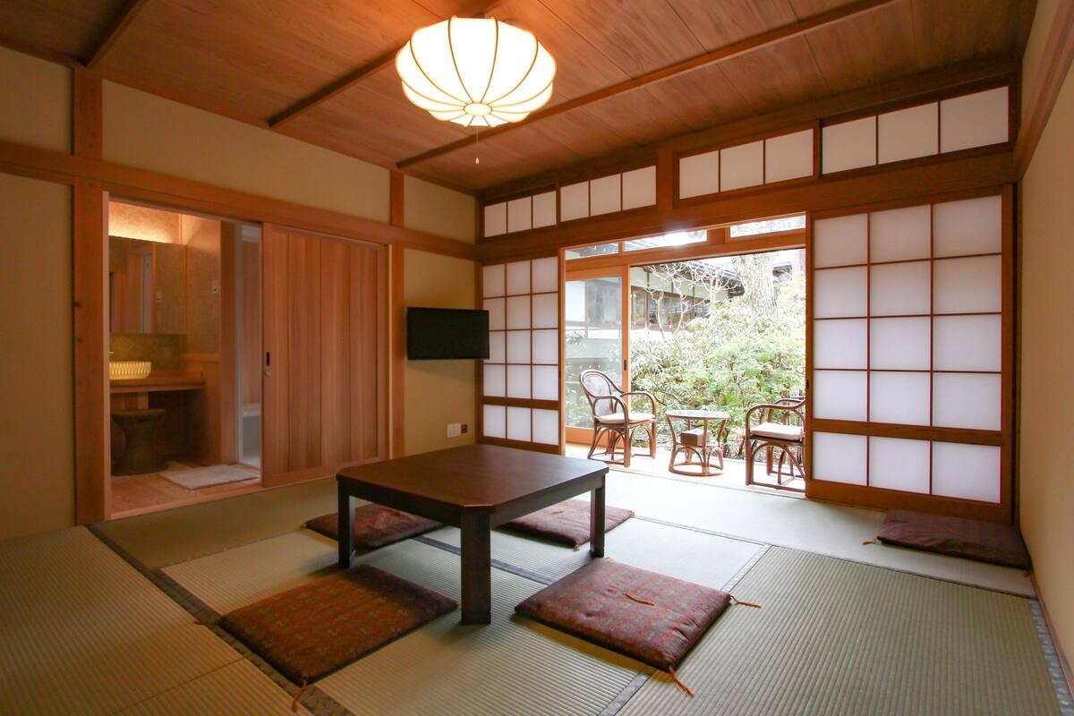 A traditional Japanese room with tatami flooring, a low table, and sliding doors leading to a garden.
