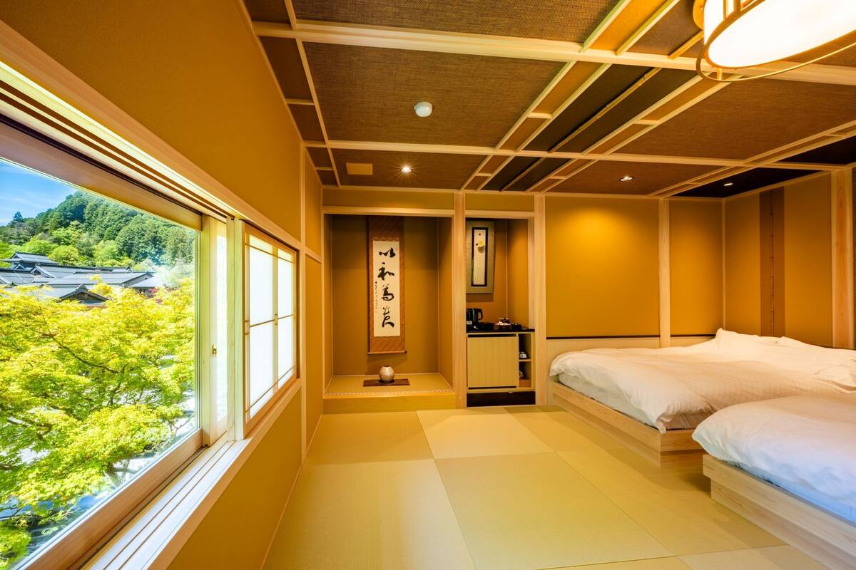 A traditional Japanese room with tatami flooring, a futon bed, a small washbasin, and a view of a forested area.