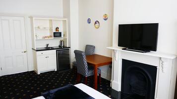 A hotel room with a bed, a desk with a chair, a television, a fireplace, and a kitchen area with a microwave and a refrigerator.