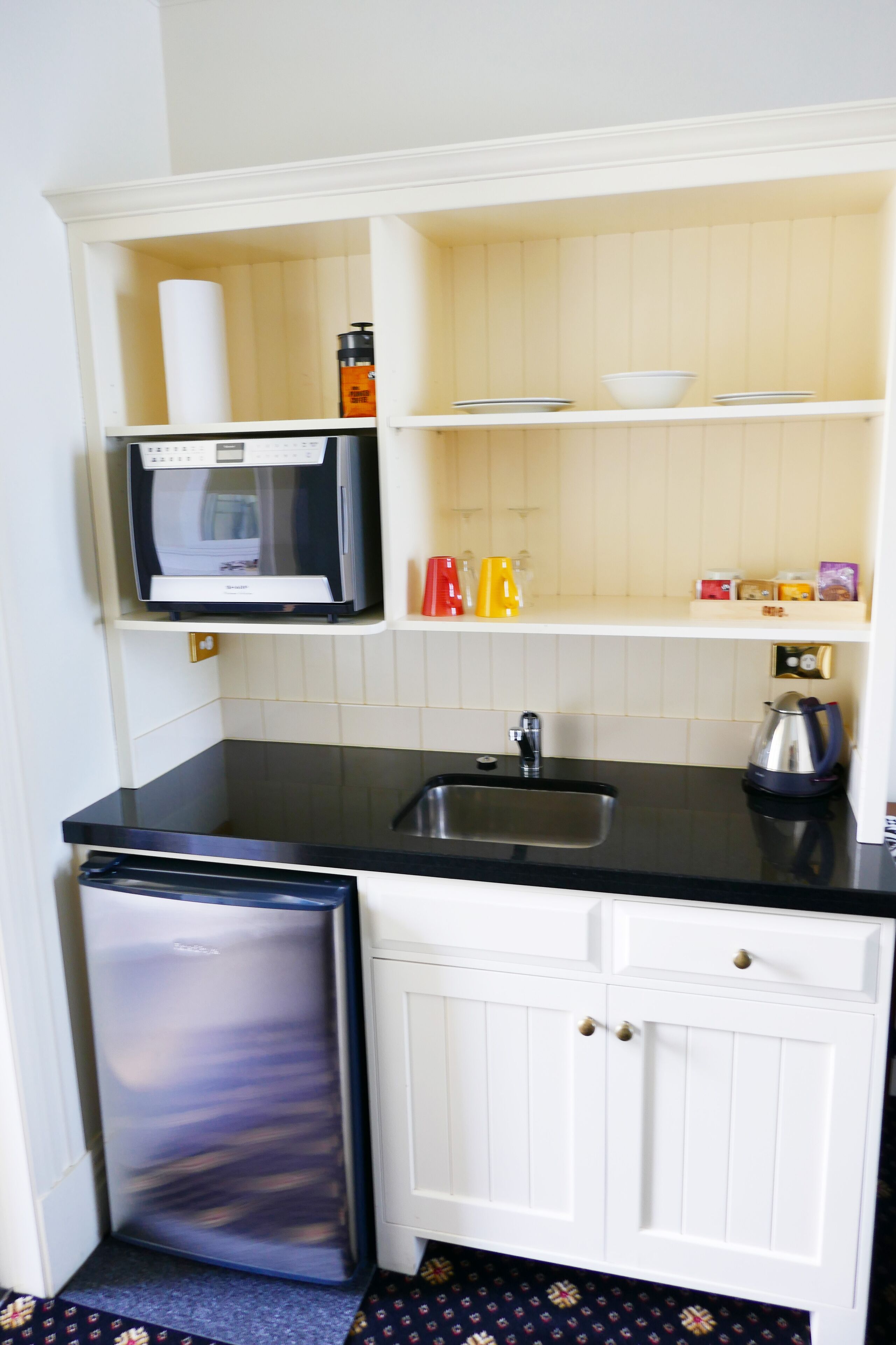 Una cocina compacta con microondas, pileta y heladera pequeña.