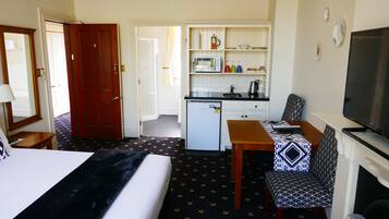 Una camera d'albergo con un letto, una scrivania, una sedia, una televisione, un angolo cottura e un bagno.