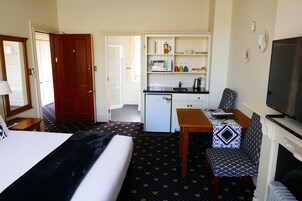 Habitación de hotel con cama, escritorio, silla, televisor, kitchenette pequeña y baño.