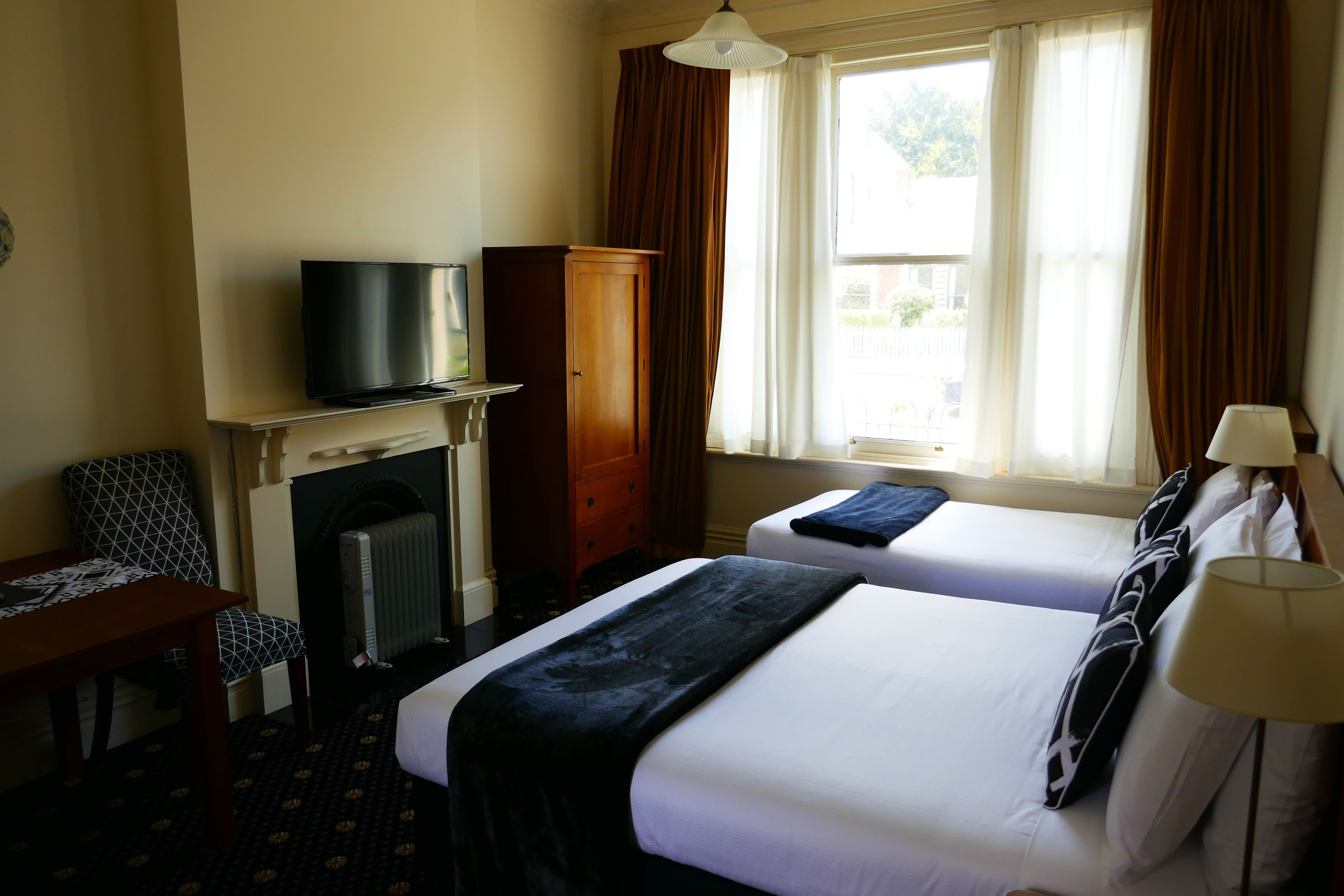 Habitación de hotel con dos camas, televisión, chimenea y ventana con cortinas.