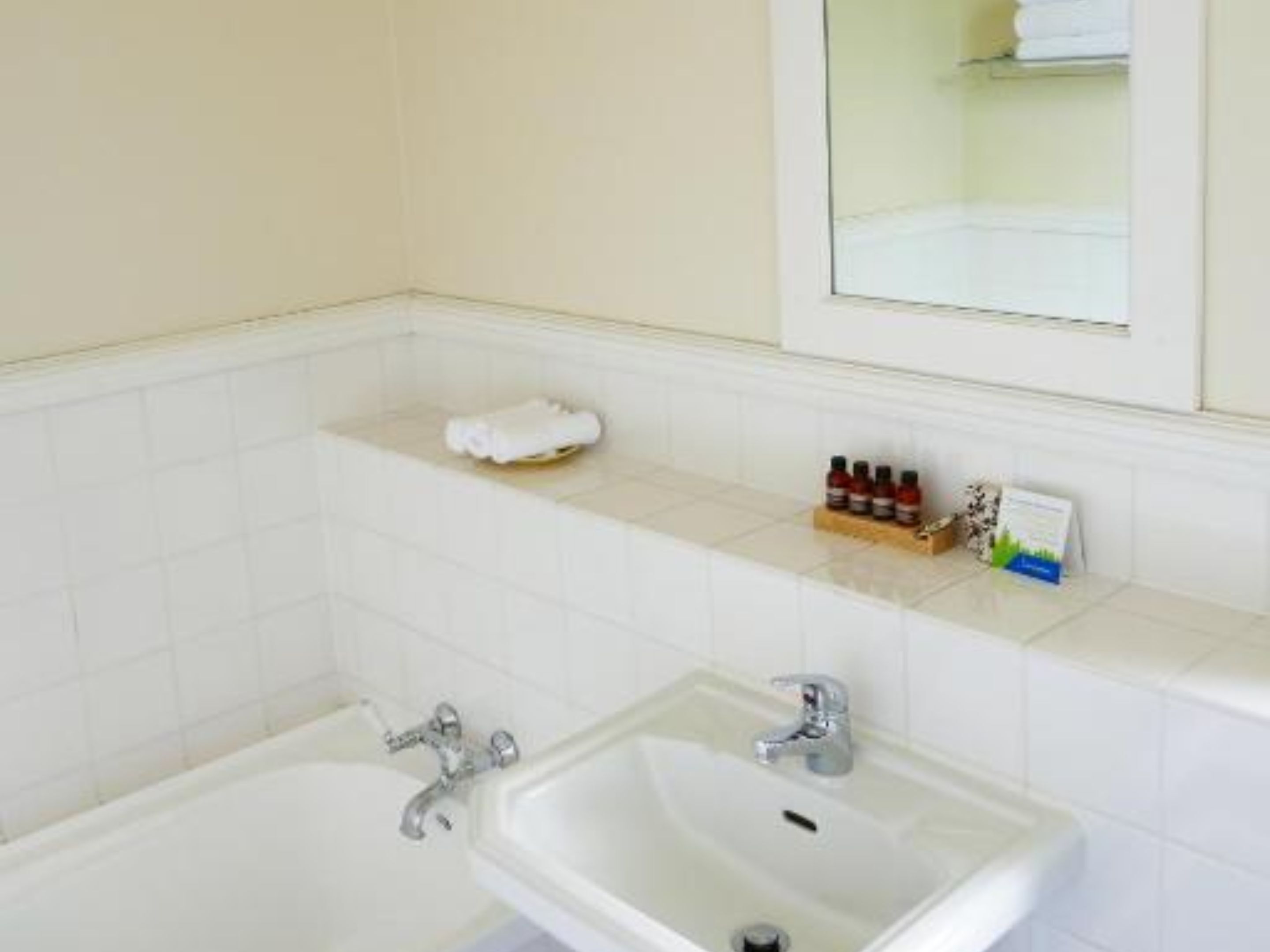 Une salle de bain avec une baignoire, un lavabo et un miroir. On y trouve un porte-serviettes et une étagère avec des articles de toilette.