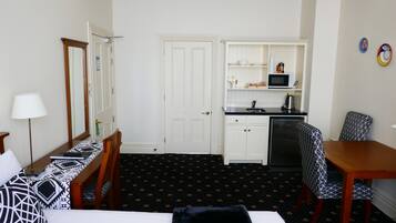 Et hotelværelse med seng, skrivebord, stol, mikroovn og et lille tekøkken.