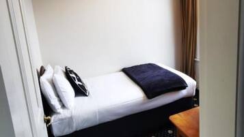 A small, single-bed room with a white bed, a dark blanket, and a black pillow.