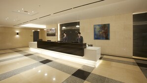 A modern reception area with a check-in counter, two staff members, and a large abstract painting on the wall. - Hotel Prumir (Hwaseong)