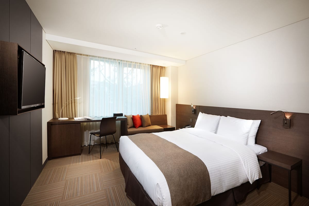 Une chambre d’hôtel avec un grand lit, un bureau avec une chaise, une télévision et une fenêtre avec des rideaux.