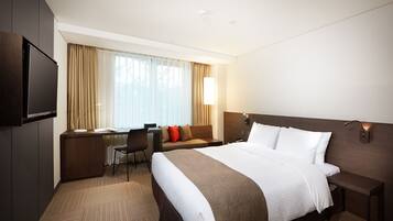 A hotel room with a large bed, a desk with a chair, a TV, and a window with curtains.